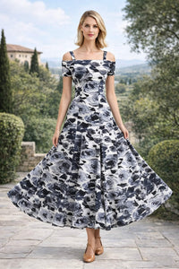 Full-length front view of a woman posing with the wide, flared skirt of a black and white floral print off-the-shoulder A-line maxi dress spread out, paired with tan Mary Jane heels.