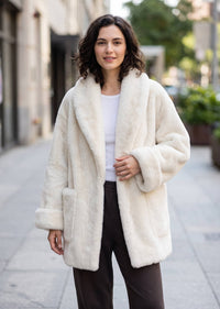 Front three-quarter look highlighting the plush texture, wide cuffs, and patch pockets on the off-white faux fur coat.   