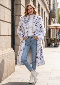Full-body outdoor look of a woman with hands in jean pockets styling a white and black snow leopard faux fur long coat. 