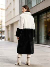 Rear view of a woman wearing a cream white and black color-block notch lapel faux fur long winter coat outdoors.