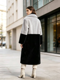 Back view of a model wearing a grey and black color-block notch lapel faux fur long coat looking over her shoulder.