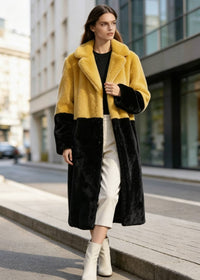 Model walking forward on the street in a mustard yellow and black two-tone plush faux fur long winter coat.
