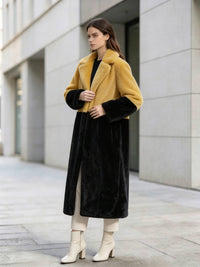 Three-quarter pose of a woman wearing a mustard yellow and black color-block notch lapel faux fur long coat outside.