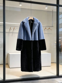 Slate blue and black two-tone notch lapel plush faux fur long coat displayed in a store window.