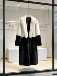 Cream white and black two-tone notch lapel plush faux fur long coat hanging on a wooden hanger in a boutique window.