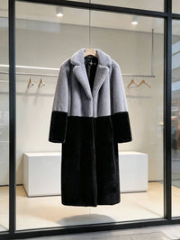 Grey and black color-block notch lapel faux fur long winter coat displayed on a hanger in a store window.
