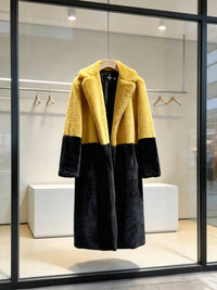 Yellow and black two-tone notch lapel plush faux fur long coat displayed in a modern boutique window.