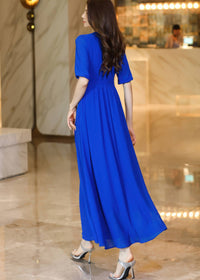 Rear profile view of a woman in a royal blue chiffon midi dress, emphasizing the elegant drape of the fabric and the half-sleeve detail.
