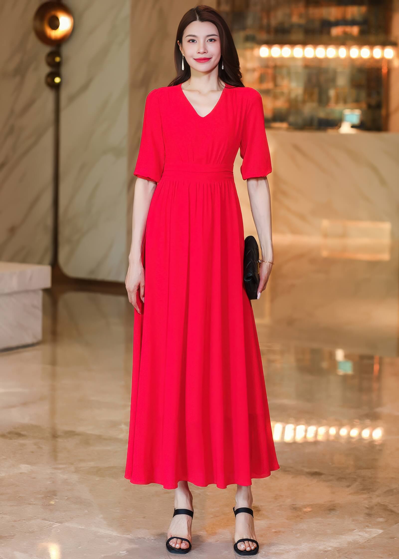 Front full-length view of a woman wearing a vibrant red V-neck chiffon midi dress with half-sleeves and a pleated skirt, paired with black strappy heels and a black clutch.