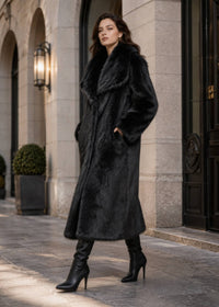 Side view of model walking in a Vivian Seven longline black faux fur coat with hands in pockets and high-heeled boots