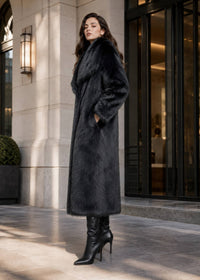 Side profile view of a women's long black plush faux fur coat with side pockets and wide collar