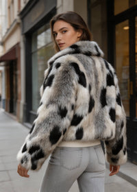 Back view of a female model wearing a cream and black spotted cropped faux fur coat styled with light gray jeans.
