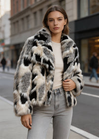 Three-quarter side view of a woman wearing a black and cream spotted cropped faux fur jacket outdoors.