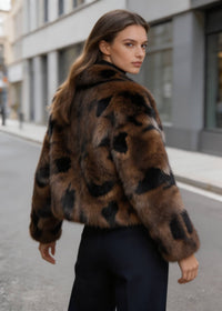 Back view of a female model wearing a brown and black spotted cropped faux fur jacket on a city street.