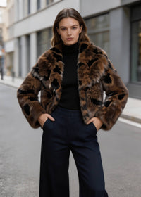 Front view of a model posing in a brown abstract leopard print cropped faux fur jacket with navy trousers.