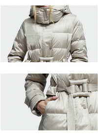 A light beige puffer coat with a hood and a matching fabric belt, shown in a split close-up view. The top panel shows the upper torso with the hood up, and the bottom panel shows a hand reaching into the front pocket.