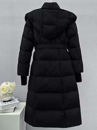 The back view of the long black puffer coat on a hanger, highlighting the horizontal quilting pattern and a large, structured hood.