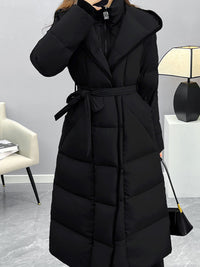 A close-up shot of the torso area of the black puffer coat, focusing on the tied waist belt, the side pocket detail, and the silver zipper at the neckline.