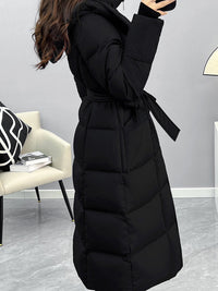A side-angle view of a woman wearing the belted black puffer coat, showing the depth of the quilting and the way the fabric belt ties at the waist.