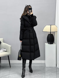 A similar full-length photo of the woman in the belted black puffer coat, this time holding a small black handbag with gold hardware.