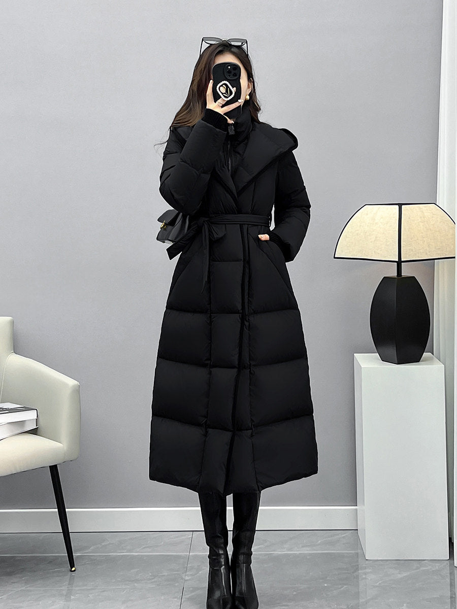 A straight-on full-body shot of the woman wearing the black puffer coat tied at the waist, styled with sunglasses on her head and pointed-toe boots.