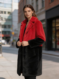 Front pose of a woman holding lapels of a red and black colorblock notch lapel faux fur coat.