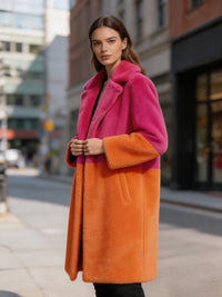 Woman posing outdoors in a vibrant pink and orange colorblock notch lapel faux fur long coat.