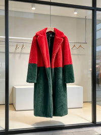 Red and dark green bold statement colorblock faux fur long coat hanging inside a modern boutique window display.