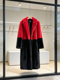 Red and black two-tone notch lapel plush faux fur long coat displayed on a hanger in a store window.