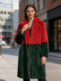 Close-up of a model posing in a red and dark green colorblock faux fur long winter coat on a city street.