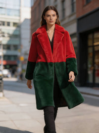 Model walking forward on a city sidewalk wearing a red and dark green colorblock plush faux fur long coat.