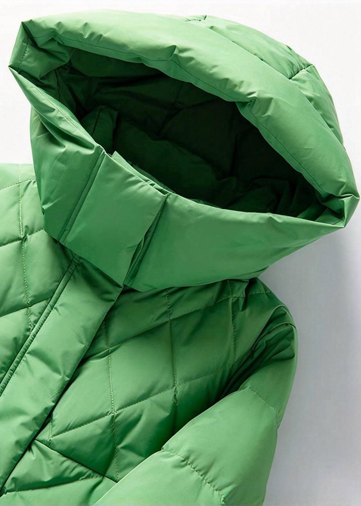 A close-up of a green quilted puffer jacket with a large hood, showing the padded stitching and fabric texture against a light gray background.