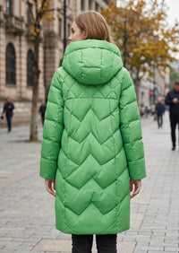 A woman viewed from behind wearing a bright green hooded puffer coat with a quilted chevron pattern, standing on a city street.