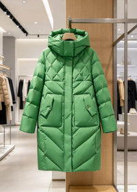 A bright green quilted puffer coat with a hood and front pockets, hanging on a wooden hanger inside a modern clothing store.