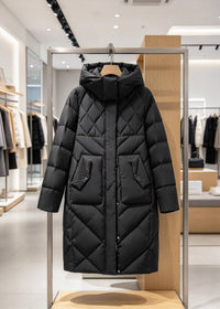 A long black quilted puffer coat with a hood and front pockets, displayed on a metal rack inside a modern clothing store.