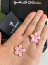 A pair of pink enamel flower drop earrings with gold-toned trim held in the palm of a hand, with the black VIVIAN SEVEN box blurred in the background.