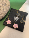 Four enamel flower drop earrings, two pink and two black, with gold-toned trim, resting on top of a small black drawstring pouch with the VIVIAN SEVEN logo.