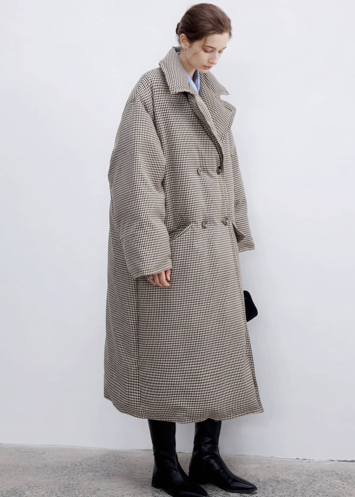 Three-quarter side full-body view of a model wearing a long double-breasted plaid down maxi coat styled with knee-high black leather boots.