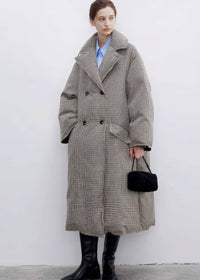 Full-length front view of a woman styled in a buttoned double-breasted plaid down maxi coat with wide notched lapels and black leather boots.