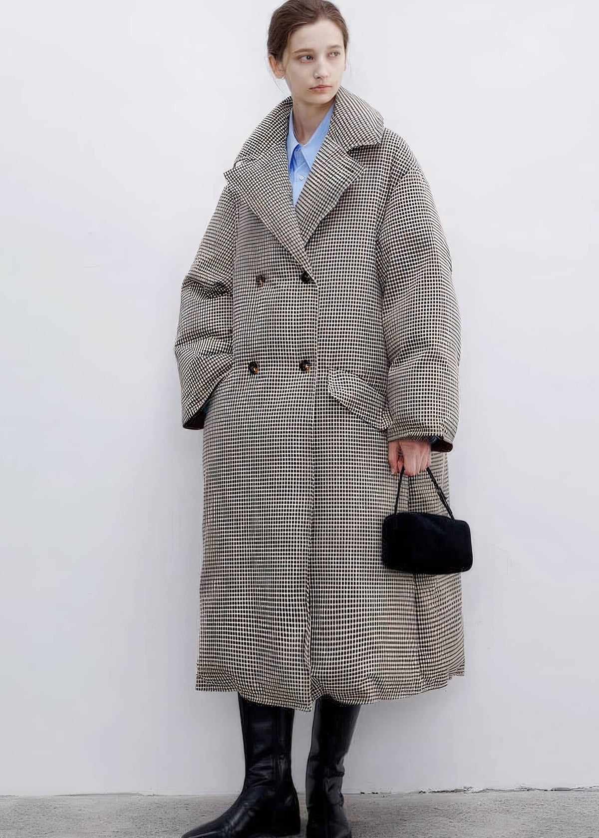 Full-length front view of a woman styled in a buttoned double-breasted plaid down maxi coat with wide notched lapels and black leather boots.