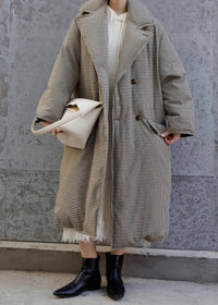 Cropped full-body street-style shot of a woman wearing an oversized plaid down maxi coat over a knit dress and carrying an off-white handbag.
