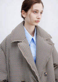 Close-up view of the double-breasted plaid down maxi coat showing collar lapels, button details, and light blue button-down shirt.
