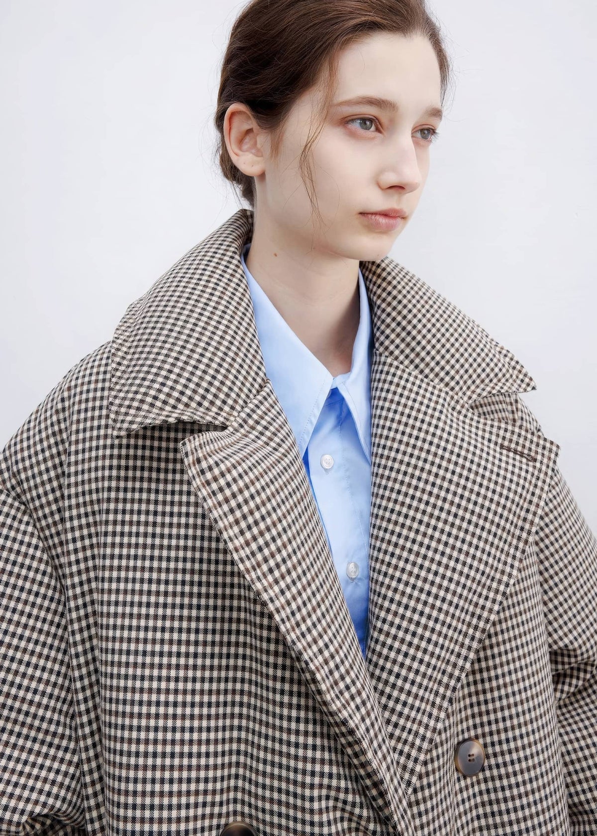 Close-up view of the double-breasted plaid down maxi coat showing collar lapels, button details, and light blue button-down shirt.