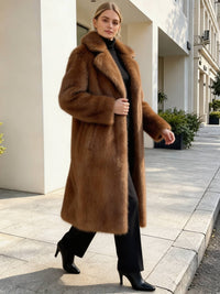 Side profile of a woman walking outdoors in a stylish long brown faux fur coat with black high heels.