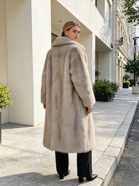 Back view of a woman wearing a long grey-beige plush faux fur coat with a large notched collar.