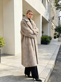 Side angle of a model posing in a long light grey plush faux fur winter coat with crossed arms.
