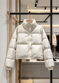 A cream-colored puffer jacket hanging on a wooden hanger from a black clothing rack inside a modern retail store.
