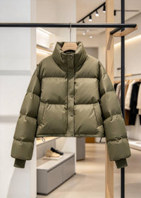 An olive green puffer jacket hanging on a wooden hanger from a clothing rack inside a modern, well-lit boutique.