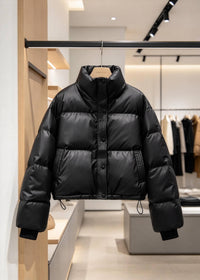 A black puffer jacket with a high stand-up collar and front snap closure, hanging on a black rack bar inside a modern clothing store.