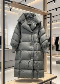 A long, puffer-style hooded coat in a muted gray-green tone hanging on a display rack inside a modern clothing store.